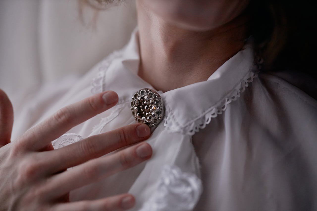 Close-up of an elegant vintage brooch pinned on a lace collar, with soft hands gently touching.